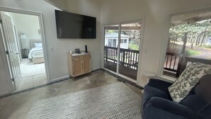 A living room with a flat-screen TV, a sofa, a wooden cabinet, and a view of a backyard through a sliding glass door.