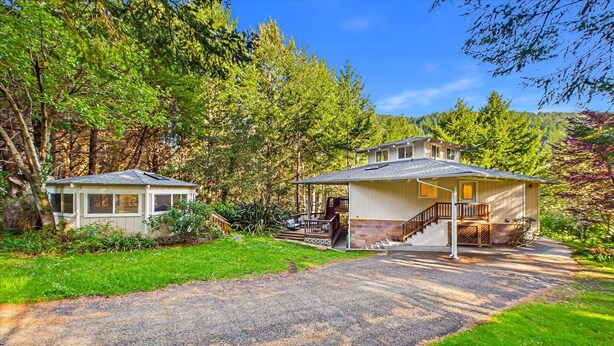 A two-story house with a covered porch and a separate garage, surrounded by a wooded area.
