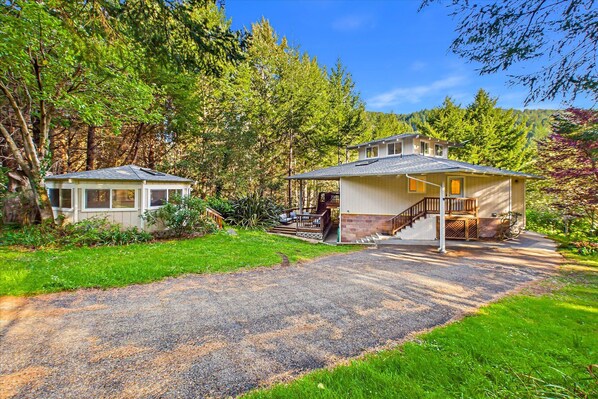 A two-story house with a covered porch and a separate garage, surrounded by a wooded area.