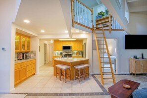 Una cocina amplia con una isla central, armarios de madera y una escalera que conduce a un nivel superior.