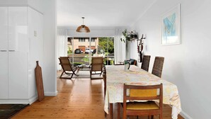 Un comedor con una mesa dispuesta para cuatro personas, sillas de madera, una lámpara colgante y vistas al exterior a través de un ventanal.