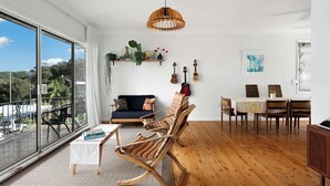 Amplia habitación con un gran ventanal, piso de madera, sofá, mesa de comedor con sillas y una lámpara colgante.
