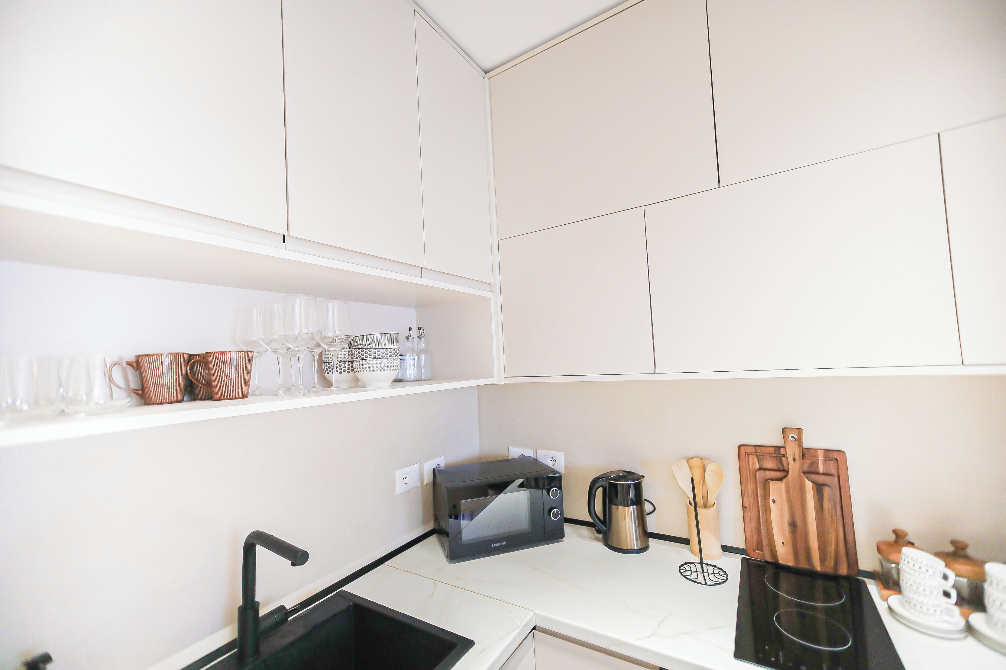 A modern kitchen with white cabinets, a black microwave, a coffee maker, and various utensils on the counter.