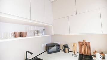 A modern kitchen with white cabinets, a black microwave, a coffee maker, and various utensils on the counter.