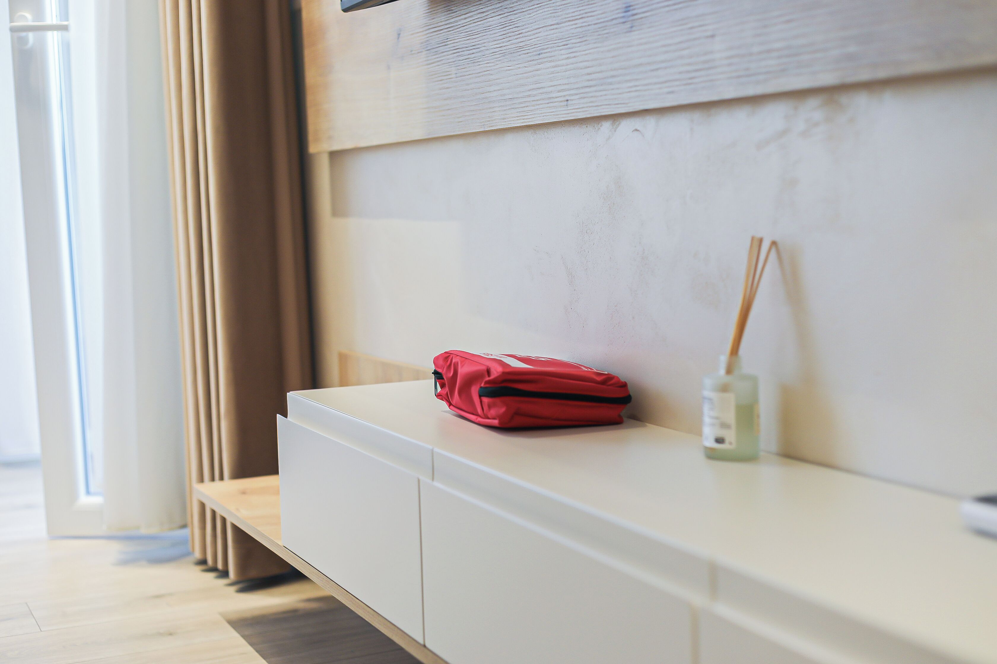 A white bedside table with a red bag and a reed diffuser.