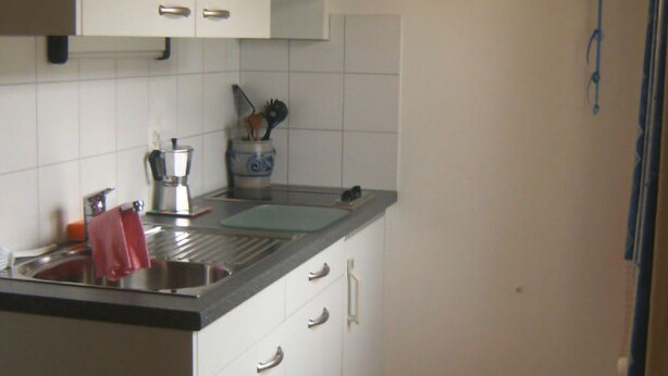 A kitchen with white cabinets, a black countertop, and a wooden ceiling.