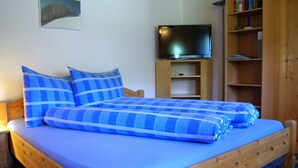 A bed with blue bedding, a television on a stand, and a bookshelf in a room with wooden walls and a ceiling.