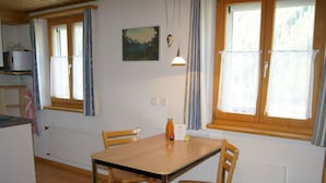 A room with a wooden table and chairs, a window with curtains, a radiator, and a painting on the wall.