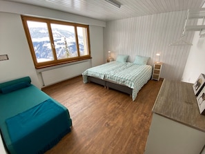 Un dormitorio con cama, ventana con vista a las montañas, mesita de noche y cómoda.