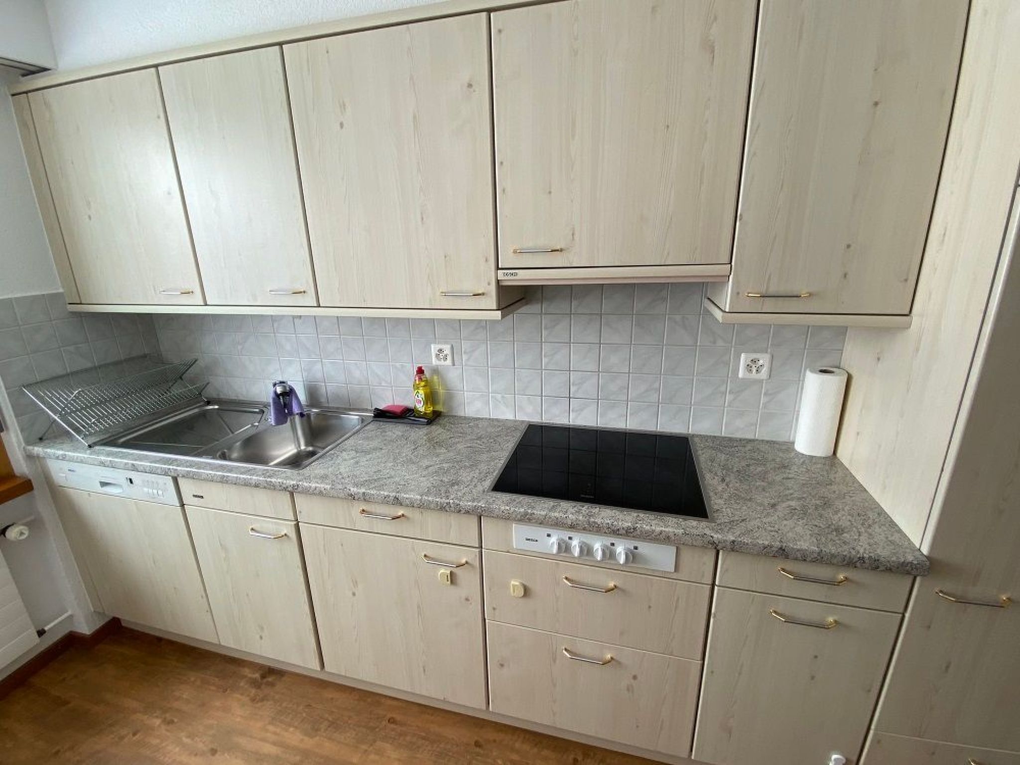 Una cocina con gabinetes de color claro, encimera de granito, pileta de acero inoxidable y estufa negra.