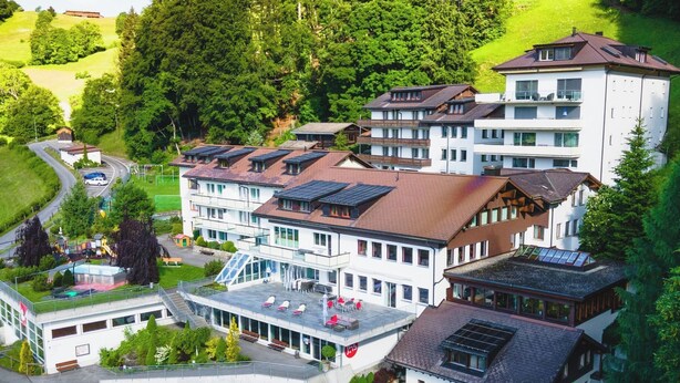 A multi-story hotel with a central courtyard, parking area, and surrounding greenery. - Ferienwohnungen JHS, (Seewis), by Interhome (Seewis im Prättigau)