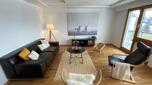 A modern living room with a black sofa, a round coffee table, and a white furry chair. - Ferienwohnungen JHS, (Seewis), by Interhome (Seewis im Prättigau)