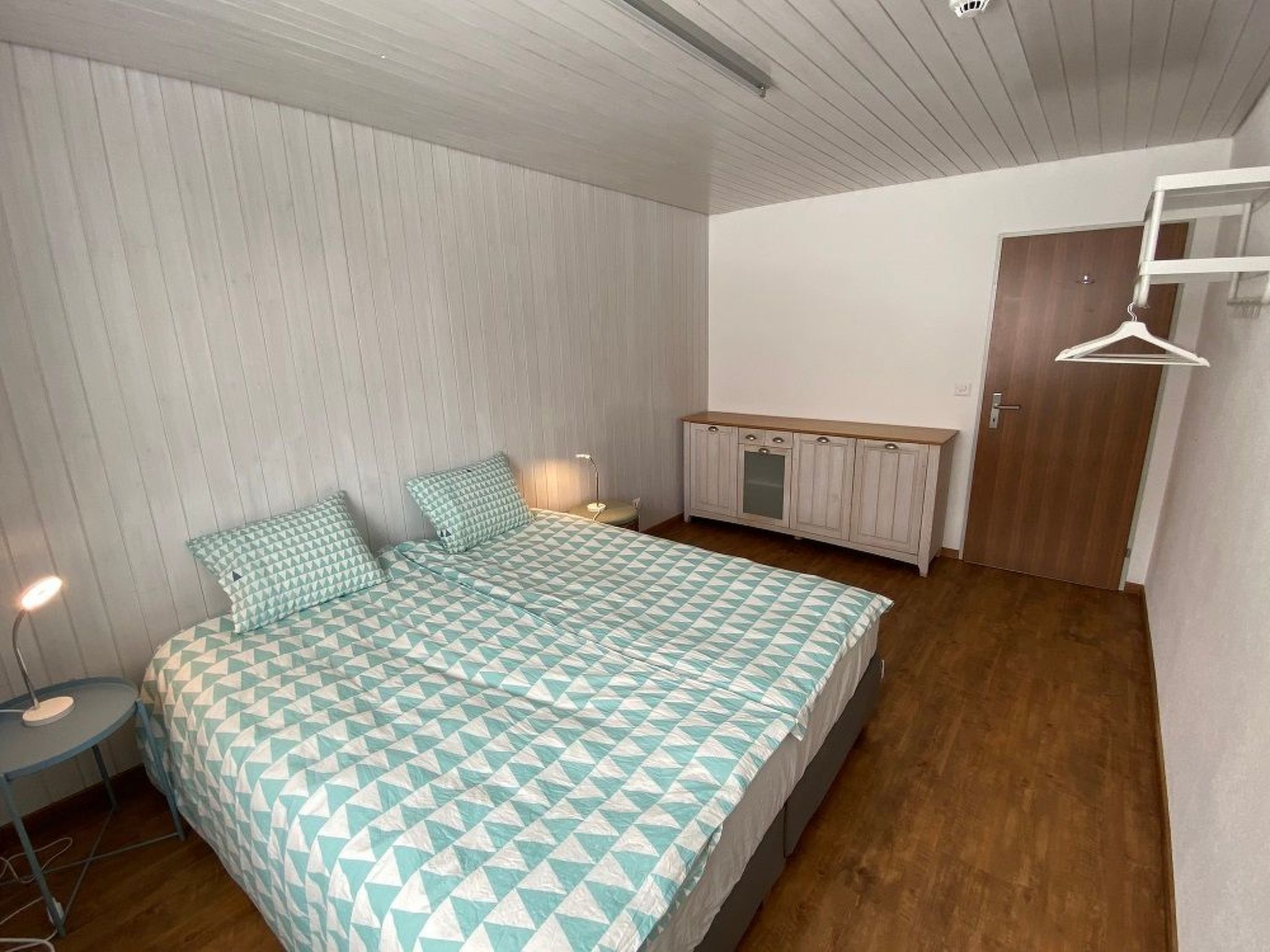 Un dormitorio con cama, mesita de noche, lámpara, armario y una puerta.