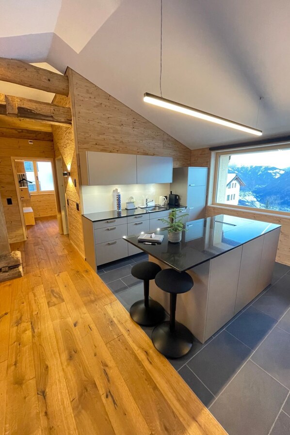 A modern kitchen with a central island, wooden flooring, and a view of mountains through large windows.
