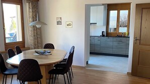 Un comedor con una mesa redonda y sillas, una cocina al fondo y suelo de madera.