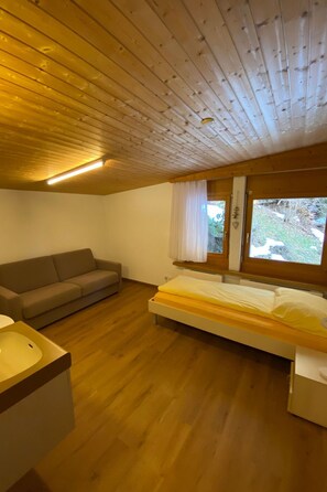 Una habitación con techo de madera, una cama con colchón, un sofá y una ventana con cortinas.