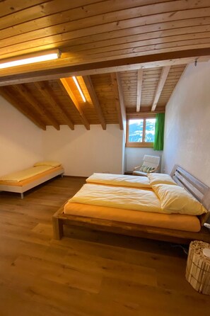 Un dormitorio con techo de madera, una cama con ropa de cama blanca, una ventana con cortinas verdes y una mesita.