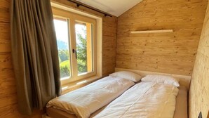 Camera da letto in una baita di legno, con un letto, una finestra e una lampada a soffitto.
