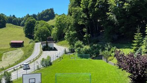 Un campo da tennis con una rete, un canestro da basket e un piccolo edificio sullo sfondo.