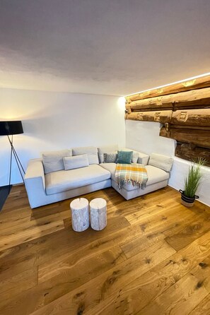 Un salon moderne avec un canapé d’angle, deux tabourets en bois, une lampe sur pied et un mur recouvert de bois.