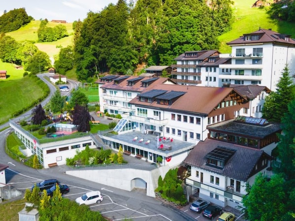 Un hotel de varios pisos con un patio central, paneles solares en el techo y un estacionamiento.