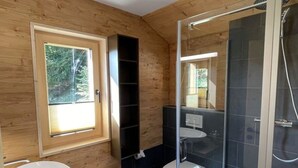 Un bagno moderno con finiture in legno, box doccia in vetro e un'ampia finestra che permette l'ingresso di luce naturale.