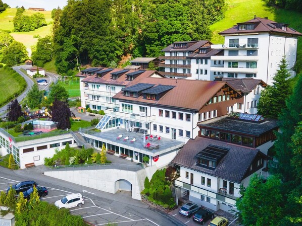 A multi-story hotel with a central courtyard, parking area, and surrounding greenery.