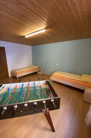 Una habitación con mesa de fútbol, dos camas y techo de madera.