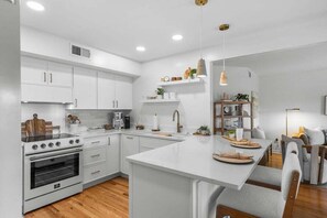 A modern kitchen with white cabinets, a central island, and a dining area with a wooden table and chairs. - Charming 2BR/2BA Courtside Villa, near Equestrian Center and Tennis. (Seabrook Island)
