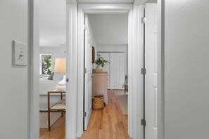 Un pasillo con piso de madera, paredes blancas y una puerta que da a otra habitación.