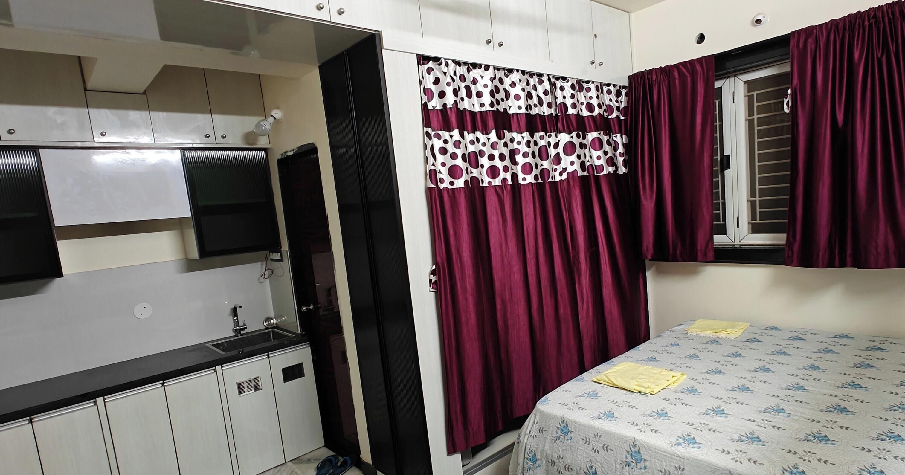 A bedroom with a bed, a window with curtains, a wardrobe, and a sink.
