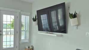Un salón con un televisor de pantalla plana montado en la pared, un sofá gris, una cesta de mimbre y un gran ventanal corredizo.