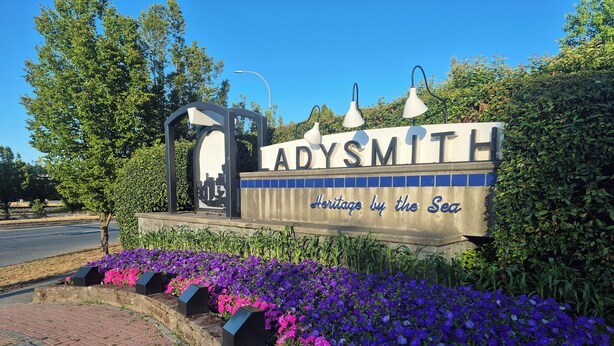 Un letrero con el texto 'ADYSMITH' y 'Heritage by the Sea', rodeado de flores moradas y rosas.