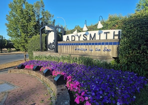 A sign with 'ADYSMITH' and 'Heritage by the Sea' text, surrounded by purple and pink flowers.