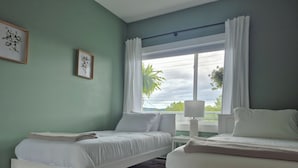 Un dormitorio con dos camas, una ventana con cortinas, una mesita de noche con lámpara y cuadros en la pared.
