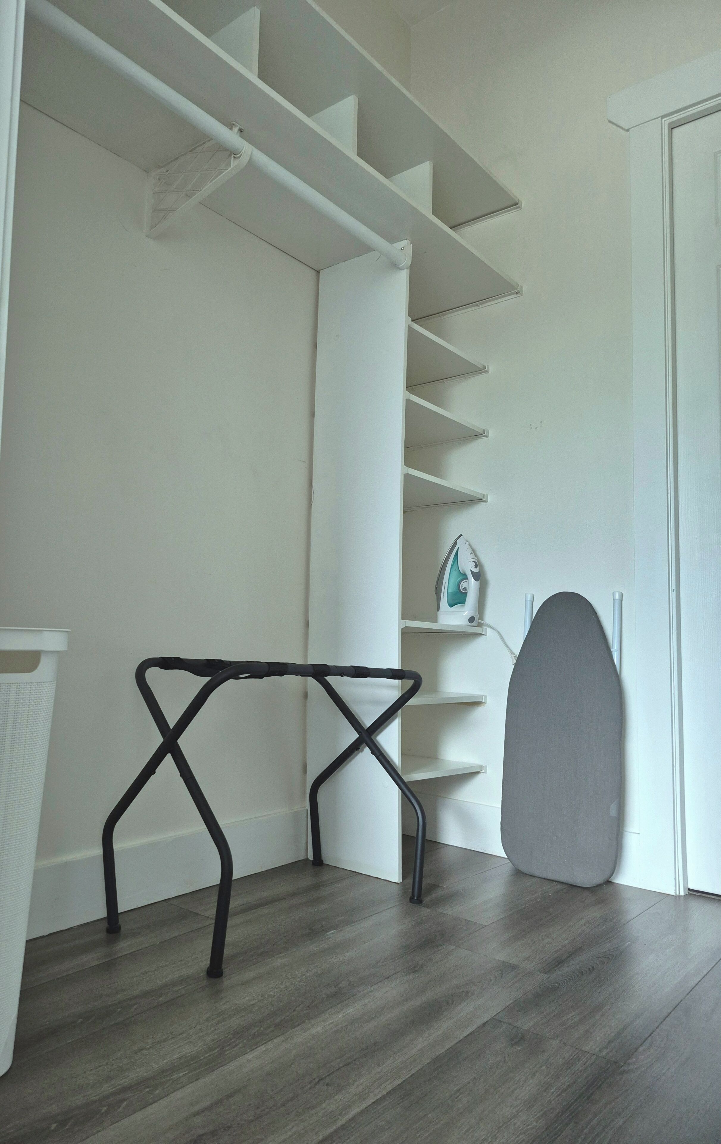 A room with a wooden floor, a white door, and a grey ironing board.