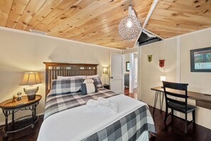 Quarto com cama, mesa de cabeceira, luminária e escrivaninha com cadeira.