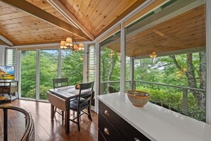 A room with a wooden ceiling, large windows, a dining table with chairs, and a white countertop with a bowl. - Cozy High Country Retreat Near the Slopes (Sugar Mountain)