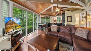 A spacious living area with a wooden ceiling, large windows, a leather sofa, and a flat-screen TV. - Cozy High Country Retreat Near the Slopes (Sugar Mountain)