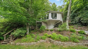 A cabin with a stone staircase leading up to a wooden deck, surrounded by lush greenery. - Cozy High Country Retreat Near the Slopes (Sugar Mountain)