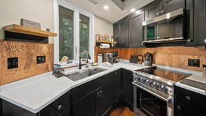 A modern kitchen with a stainless steel range, black cabinets, and a copper backsplash. - Cozy High Country Retreat Near the Slopes (Sugar Mountain)