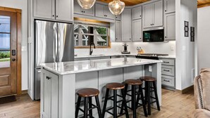 Una cucina moderna con mobili grigi, un frigorifero in acciaio inossidabile, una grande isola con sgabelli, illuminazione a sospensione e un soffitto in legno.