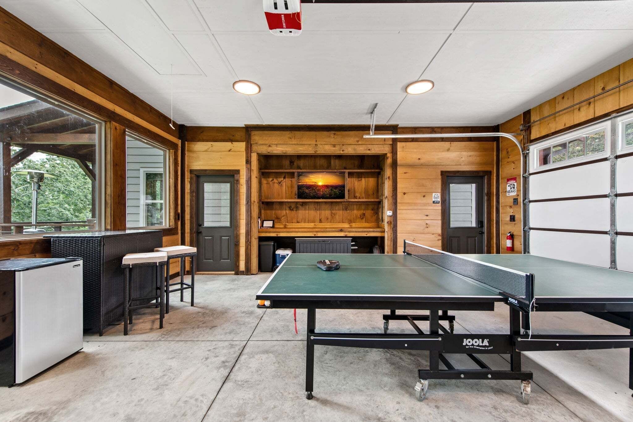 Une table de ping-pong dans une pièce dont l’intérieur est en bois, avec un réfrigérateur et une fenêtre.