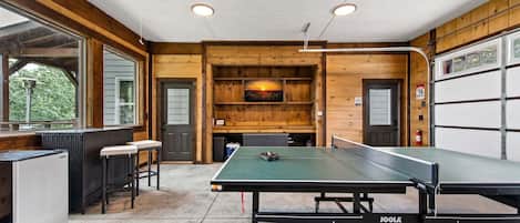 Une table de ping-pong dans une pièce dont l’intérieur est en bois, avec un réfrigérateur et une fenêtre.