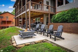 Eine überdachte Terrasse im Freien mit Adirondack-Stühlen, einer Feuerstelle und einem Grill.
