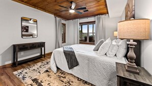 Una camera da letto con un letto, una ventola a soffitto, un comodino, una lampada, uno specchio e una finestra con tende.