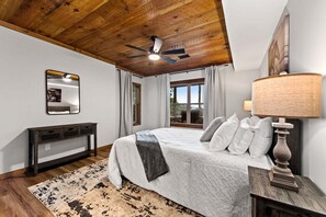 Ein Schlafzimmer mit Bett, Deckenventilator, Nachttisch, Lampe, Spiegel und einem fenster mit Vorhängen.