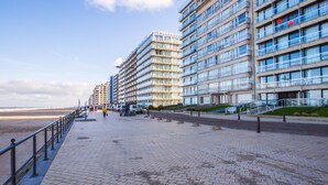 Eine Uferpromenade mit modernen Gebäuden, einem gepflasterten Gehweg und einem Strand im Hintergrund.