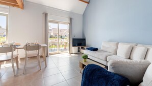 En moderne stue med sofa, tv, spisebord, stole og en skydedør til et udendørs område.