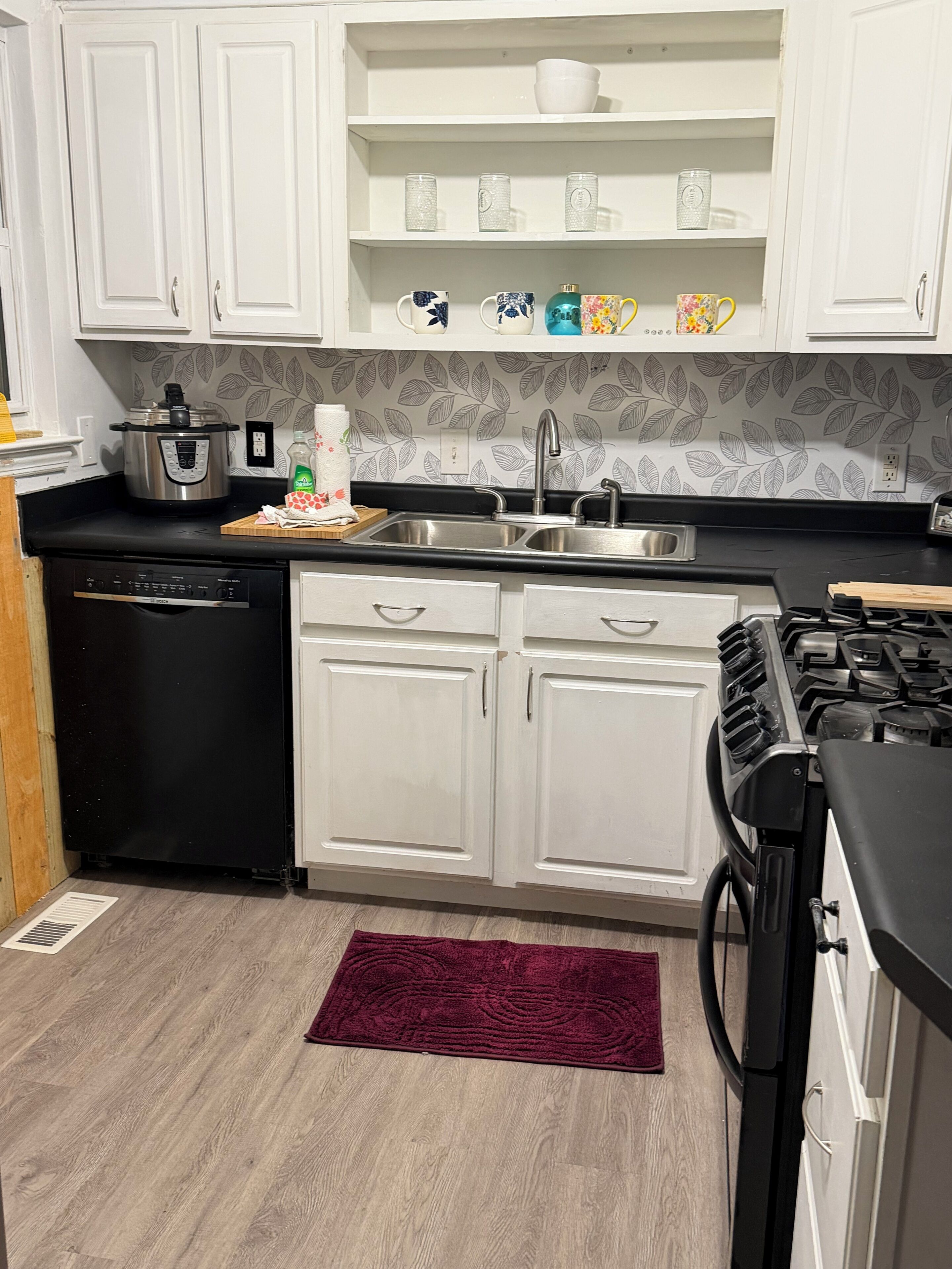 A kitchen with white cabinets, a black dishwasher, a stove, and a red rug.